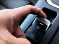Dłoń naciska przycisk elektrycznego hamulca postojowego. Pomoc w zrozumieniu, jak wyłączyć elektryczny hamulec postojowy.
