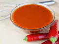 Schüssel mit leuchtend orangeroter Buffalo Sauce, daneben rote Chilis und ein Schneebesen. Perfekt für Flügel!