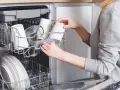 Kobieta wkłada kubki do zmywarki, pokazując, jak układać garnki i naczynia, by były czyste.