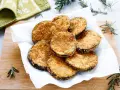 Cotolette di melanzane dorate e croccanti, servite su carta bianca con rametti di rosmarino.