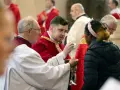 Clergy in red robes perform communion, a sacred act that can be seen as a form of evangelizing, sharing faith with a young woman.
