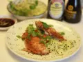 Crujiente solomillo de pollo empanado, adornado con cilantro fresco y brotes, servido con salsa y un cuenco de ensalada.