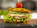 Burger z warzywną bułką, kotletem, ogórkiem, sosem i pomidorkiem na wykałaczce.
