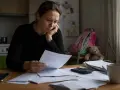 Zmartwiona kobieta przegląda dokumenty. W tle widać plecak i misia. Syndyk nie wypłaca alimentów, co pogłębia jej troski.
