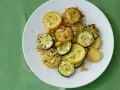 Gegrillte gelbe Zucchini-Scheiben mit Pinienkernen und Kräutern auf einem weißen Teller.
