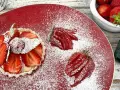 Zuckersüße Erdbeer Tartelettes, bestäubt mit Puderzucker, auf rotem Teller. Daneben frische Erdbeeren und eine Gabel.