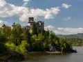 Zamek w Czorsztynie góruje nad jeziorem, otoczony zielenią. W oddali widać góry.