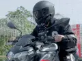 Motocyklista w kasku siedzi na motocyklu Kawasaki, z zamontowanym interkomem na kasku.
