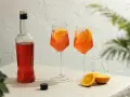 Idealny aperol spritz przepis: butelka Aperolu, dwa drinki z pomarańczą i lodem, obok połówki pomarańczy.