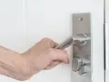 Dłoń trzymająca metalową klamkę drzwi z folią ochronną.