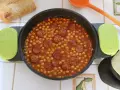 Guiso de garbanzos con chorizo en una cazuela, con pan y cuchara naranja.