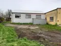 Teren wokół budynków jest nierówny, z błotnistymi śladami i trawą. Widać tu różne formy terenu, od płaskich placów po lekko nachylone trawniki.