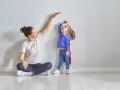 Mama mierzy wzrost córeczki w stroju superbohaterki. To właśnie wtedy dzieci rosną najszybciej, zaskakując nas każdego dnia.