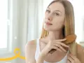 Kobieta z długimi blond włosami szczotkuje je drewnianą szczotką, dbając o oczyszczanie skóry głowy.