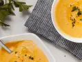 Deux bols de velouté de butternut facile, ornés d'huile d'olive et de persil frais, prêts à être dégustés.