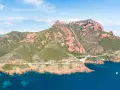 Strada panoramica sulla Corniche de l'Esterel, con montagne rosse e mare blu intenso.