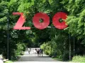 Duże czerwone litery "ZOO" nad alejką w parku. Wiele zoo w Polsce zaprasza na spacer.