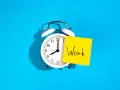 Reloj despertador blanco con nota amarilla que dice "Work", recordando la importancia de la jornada laboral.