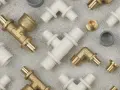 Białe złączki ppsu i mosiężne elementy hydrauliczne tworzą wzór na szarym tle.