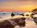 Zachód słońca nad Bałtykiem na Pomorzu Zachodnim. Fale obmywają kamienistą plażę, a niebo mieni się odcieniami pomarańczy i różu.
