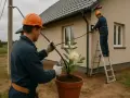 Dwóch elektryków pracuje przy domu. Jeden na drabinie podłącza kable, drugi trzyma kabel. Zastanawiasz się, ile kosztuje przyłącze prądu?