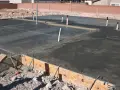 Świeżo wylana płyta fundamentowa z widocznymi rurami i zbrojeniem. Trwa izolacja pozioma fundamentów.