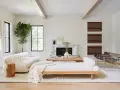 Elegante salón con decoración blanco y madera natural. Sofá curvo blanco, diván de madera, chimenea de mármol y plantas.