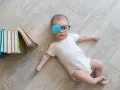 Bambino con occhiali e cerotto sull'occhio per correggere l'occhio ambliope, sdraiato vicino a una pila di libri colorati.
