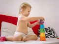 Chłopiec, 3 latek, nie mówi, ale wszystko rozumie. Z uśmiechem układa kolorowe kubeczki na łóżku.