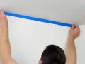 Ręce przyklejają niebieską taśmę malarską, tworząc odcięcie sufit ściana. Przygotowanie do malowania.