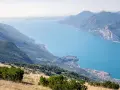 Panoramica mozzafiato del lago di Garda sponda veronese, con montagne verdi e un borgo pittoresco affacciato sull'acqua azzurra.