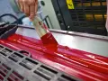 Mano esparciendo tinta roja en rodillos de imprenta, mostrando las ventajas de la imprenta para la difusión masiva de información.