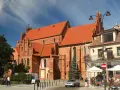 Gotycka ceglana bazylika w Tczewie, z pomarańczowym dachem, to jedna z głównych atrakcji miasta. W tle kawiarniany ogródek.