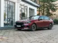 Eleganckie, matowoczerwone BMW 550e z czarnymi akcentami stoi na brukowanym podjeździe przed budynkiem z dużymi oknami.