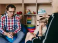Terapeuta rozmawia z dzieckiem, ćwicząc teorię umysłu. W tle zabawki i pomoce edukacyjne.