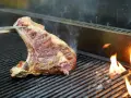 Una succulenta bistecca alla fiorentina, con la sua storia di sapori, cuoce sulla griglia tra fiamme vive e fumo.
