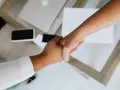 Uścisk dłoni symbolizujący podpisanie umowy na czas nieokreślony. Na stole leży laptop i dokumenty.