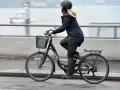 Kvinna cyklar på en elcykel, kanske med bidrag för att underlätta pendlingen. Hon bär hjälm och en varm jacka.