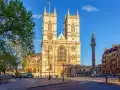 L'abbaye de Westminster, majestueuse et illuminée par le soleil, se dresse fièrement avec ses tours jumelles. Une colonne commémorative se dresse à droite.