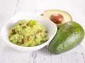 Miseczka guacamole z awokado, cebulą i papryczką chili na drewnianym tle.