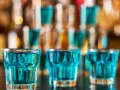 Trzy szklanki z niebieskim płynem, gotowe do wypicia jako kamikaze shot. W tle bar z butelkami.