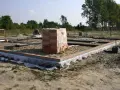 Stan zero budynku: fundamenty z cegły i betonu, piasek, folia izolacyjna, stos cegieł pod przykryciem.