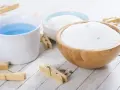 Bol en bois rempli de lessive en poudre maison, à côté d'une tasse de liquide bleu et de pinces à linge en bois.