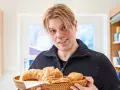 Mann mit blonden Haaren hält einen Korb mit frischen Backwaren, darunter ein Croissant und ein Kieler Semmel.