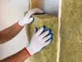 Mani guantate posizionano un pannello di lana di roccia, un materiale da **cemento isolante termico**, all'interno di una struttura in legno.