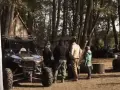 Grupa ludzi przy pojazdach terenowych podczas Polaris camping. W tle las i drewniana chata.