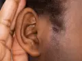 Une main couvre une oreille, comme pour mieux entendre ou se protéger du bruit. Cela peut évoquer ce qu'est-ce qui provoque des acouphènes.