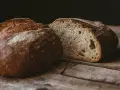 Ein rustikales, aufgeschnittenes sauerteigbrot ohne kneten liegt auf einer Holzoberfläche. Die Kruste ist dunkelbraun und knusprig, das Innere luftig und porös.