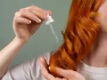 Dłoń z pipetką z olejkiem aplikuje pielęgnację na rude, falowane włosy. Dowiedz się, jak często olejować włosy dla najlepszych efektów.