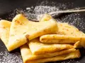 Deliciosos crepe en francés, doblados y espolvoreados con azúcar glas sobre un plato negro.